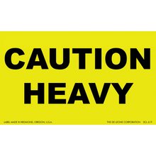 Yellow warning sign with black text reading ’CAUTION HEAVY’