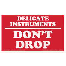 Red warning label with white text reading ’DELICATE INSTRUMENTS DON’T DROP’