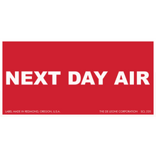 Red shipping label with white text reading ’NEXT DAY AIR’